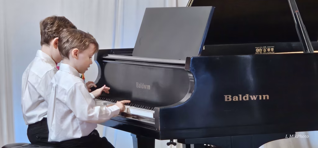 Two children playing a piano duet during their recital at K&M Music Company in San Diego